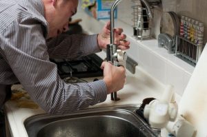 A plumber fixing a faucet with kitchen water damage